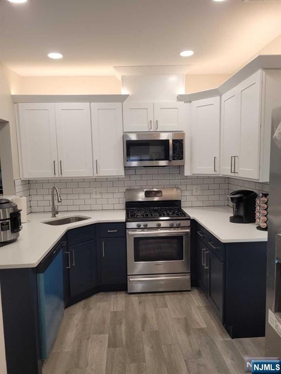 kitchen with light wood finished floors, a sink, stainless steel appliances, light countertops, and backsplash