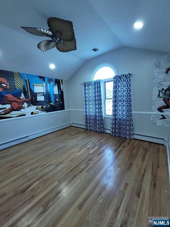 interior space with a baseboard heating unit, vaulted ceiling, wood finished floors, and visible vents