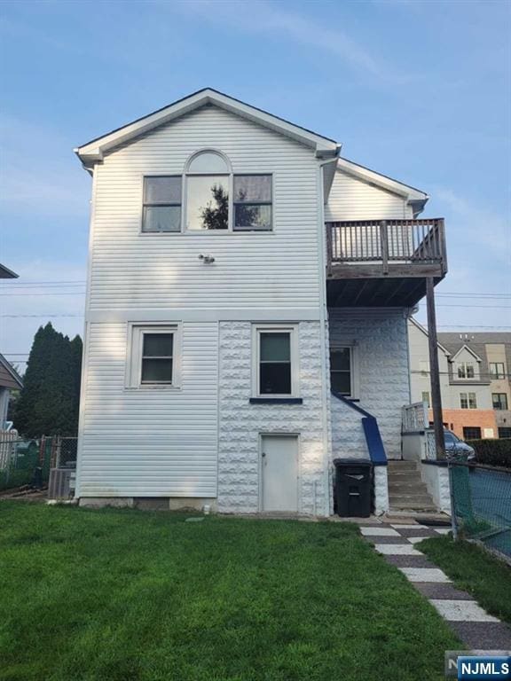 rear view of house with a yard, a balcony, and fence