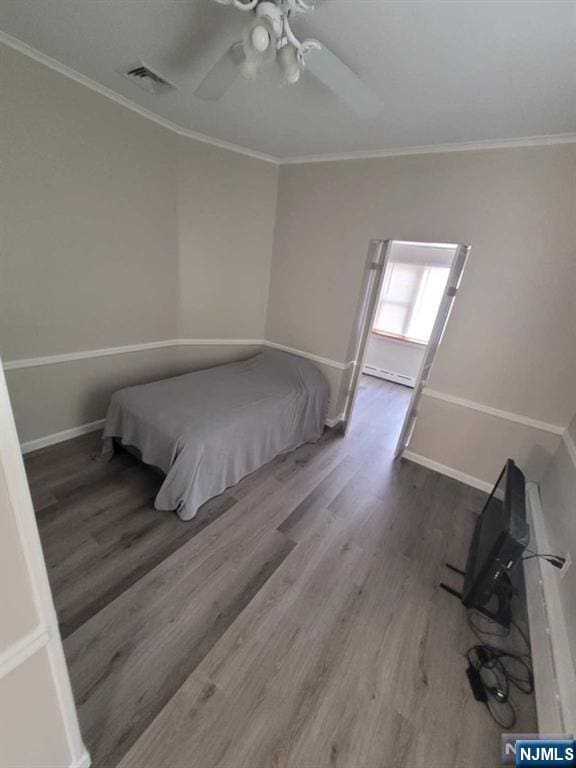 bedroom featuring a baseboard heating unit, wood finished floors, visible vents, baseboards, and ornamental molding