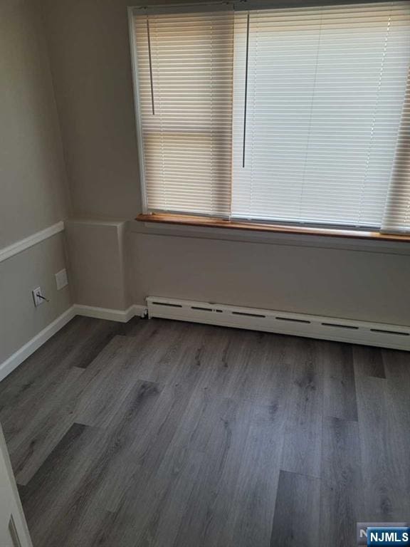 empty room with baseboards, baseboard heating, and wood finished floors