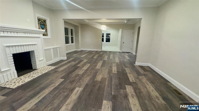 unfurnished living room with dark wood-type flooring, a brick fireplace, and baseboards