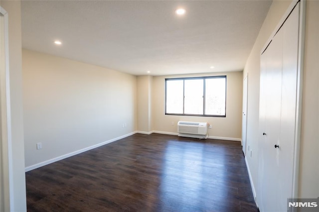 unfurnished room featuring recessed lighting, baseboards, dark wood-type flooring, and a wall unit AC