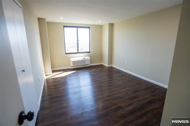 empty room featuring a wall mounted air conditioner, baseboards, dark wood-style floors, and recessed lighting