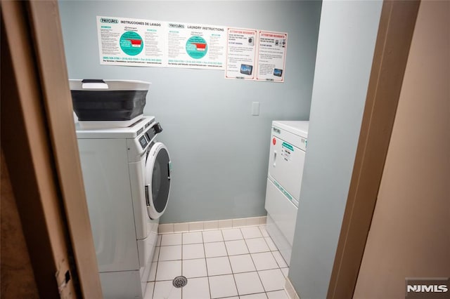 laundry room featuring washer and clothes dryer, light tile patterned floors, and baseboards