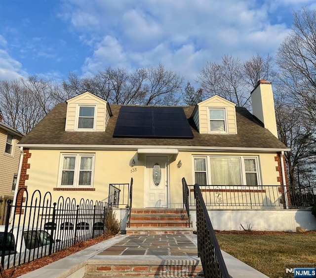 view of front of home with a fenced front yard, a chimney, solar panels, and stucco siding