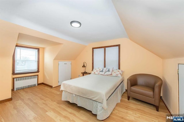 bedroom with baseboards, vaulted ceiling, light wood-style flooring, and radiator heating unit