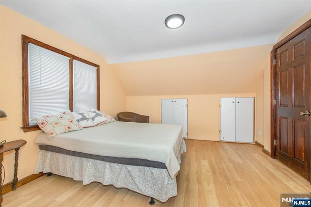 bedroom featuring lofted ceiling, light wood-type flooring, and baseboards