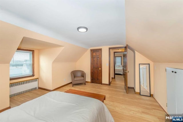 bedroom with radiator, light wood-type flooring, baseboards, and lofted ceiling