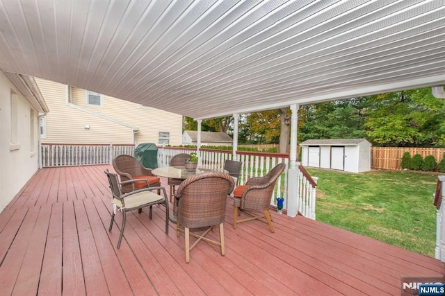 wooden deck featuring outdoor dining area, a lawn, fence, a shed, and an outdoor structure