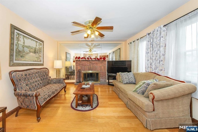 living room featuring a ceiling fan, a brick fireplace, baseboards, and wood finished floors