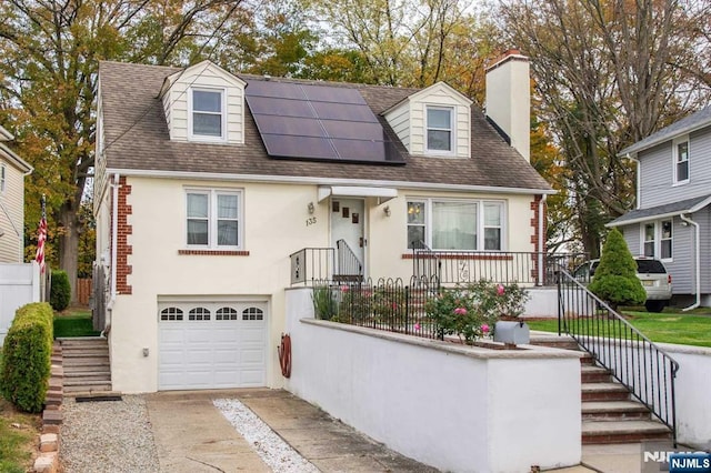 cape cod home with a chimney, stucco siding, roof mounted solar panels, fence, and driveway