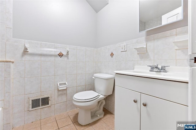 bathroom with visible vents, toilet, tile patterned flooring, vanity, and tile walls