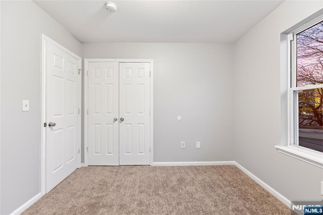 unfurnished bedroom featuring a closet, multiple windows, carpet flooring, and baseboards