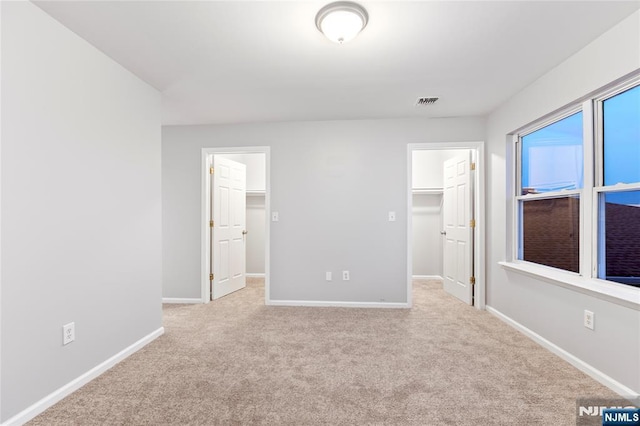 unfurnished bedroom with a walk in closet, carpet, and baseboards