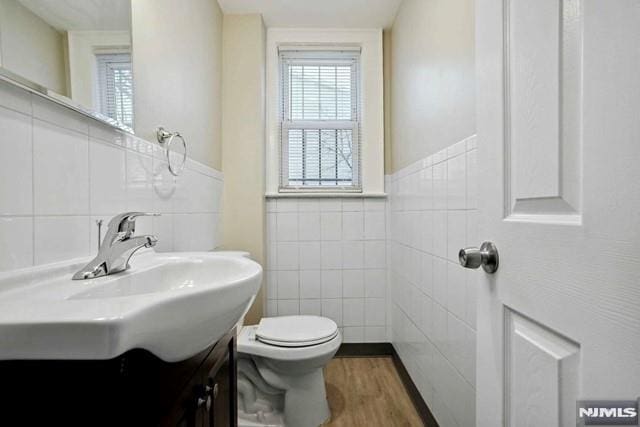 bathroom featuring toilet, tile walls, wood finished floors, and vanity