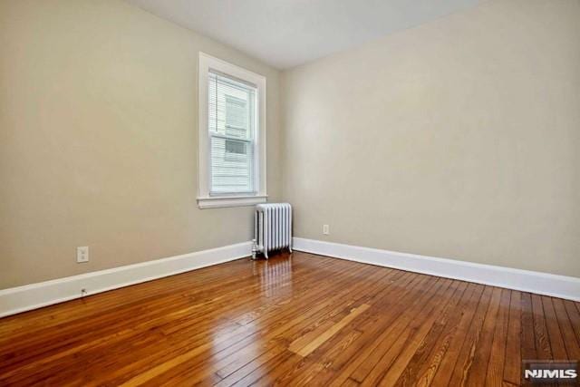 unfurnished room with hardwood / wood-style flooring, radiator, and baseboards