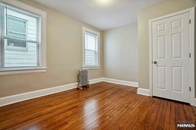 empty room with radiator heating unit, baseboards, and wood-type flooring