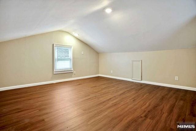 bonus room featuring dark wood-type flooring, baseboards, and vaulted ceiling