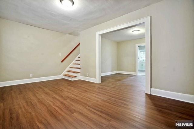 empty room featuring stairway, baseboards, and dark wood-type flooring