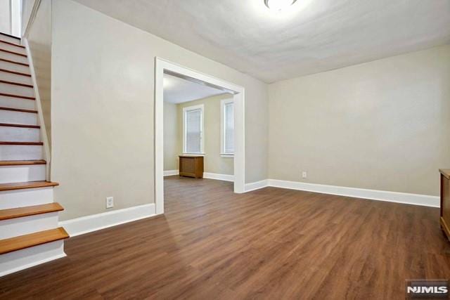 spare room with stairway, baseboards, and dark wood-style floors