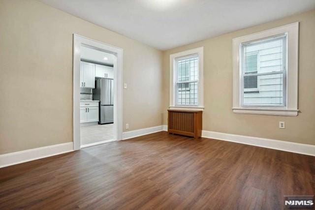 empty room with dark wood-style floors, radiator heating unit, and baseboards