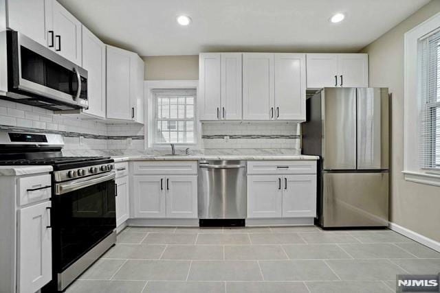 kitchen featuring backsplash, white cabinets, stainless steel appliances, and a sink