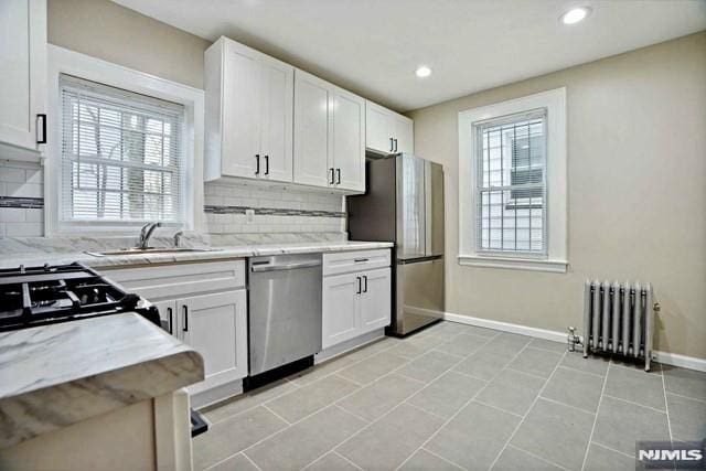 kitchen with a sink, stainless steel appliances, radiator heating unit, and white cabinetry