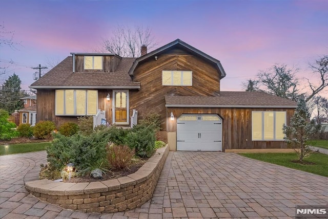 view of front of property featuring decorative driveway, roof with shingles, and a chimney