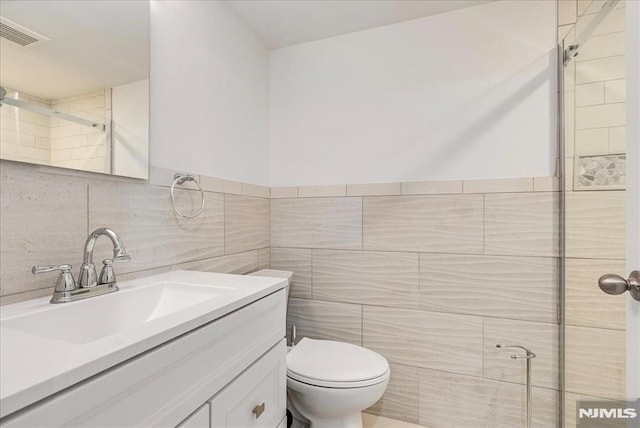 bathroom featuring vanity, tile walls, toilet, and visible vents