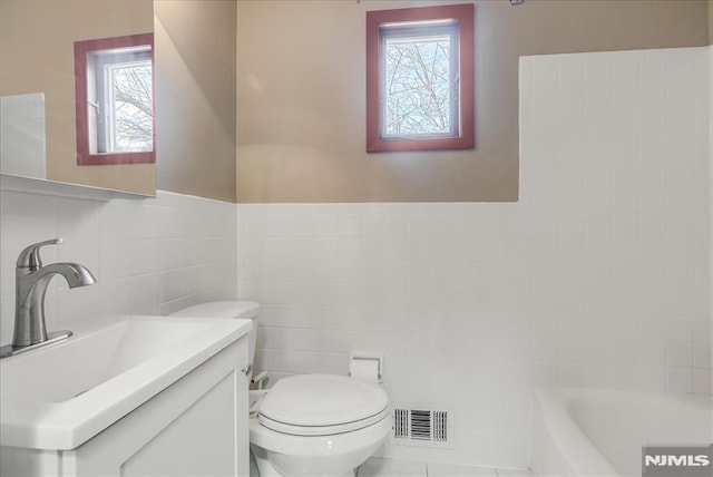 bathroom featuring visible vents, toilet, a bathing tub, tile walls, and vanity