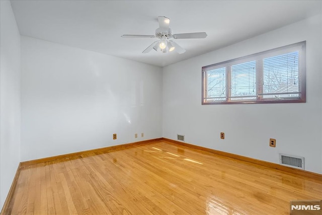 spare room featuring visible vents, baseboards, hardwood / wood-style floors, and a ceiling fan