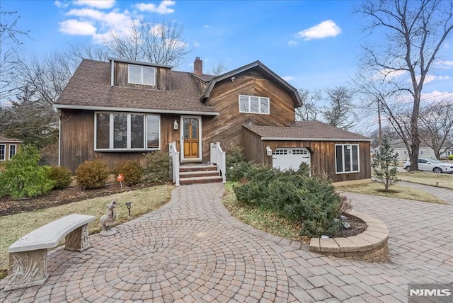 view of front of property featuring a garage, a chimney, and roof with shingles