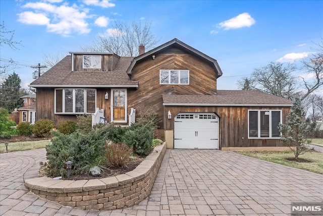 tri-level home featuring a garage, a chimney, decorative driveway, and roof with shingles