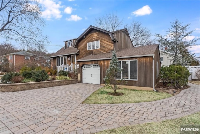 split level home featuring decorative driveway, a garage, and roof with shingles