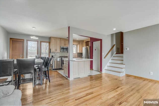 kitchen with a kitchen island, light wood-style flooring, stainless steel appliances, light countertops, and backsplash