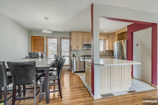 kitchen featuring a kitchen island, stainless steel appliances, decorative backsplash, light countertops, and light wood-style floors