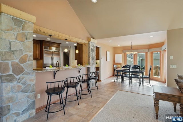 kitchen featuring high vaulted ceiling, light stone counters, a breakfast bar, built in refrigerator, and hanging light fixtures