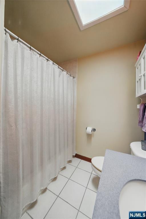 full bathroom featuring a skylight, baseboards, toilet, tile patterned floors, and a sink