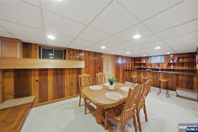 dining space with light carpet, wooden walls, a bar, and recessed lighting