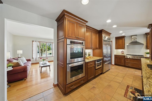 kitchen with stainless steel appliances, recessed lighting, open floor plan, wall chimney range hood, and light stone countertops