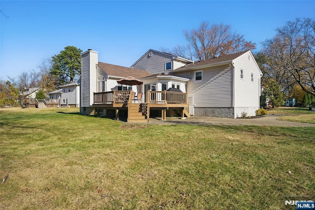 rear view of property with a chimney, a deck, and a yard