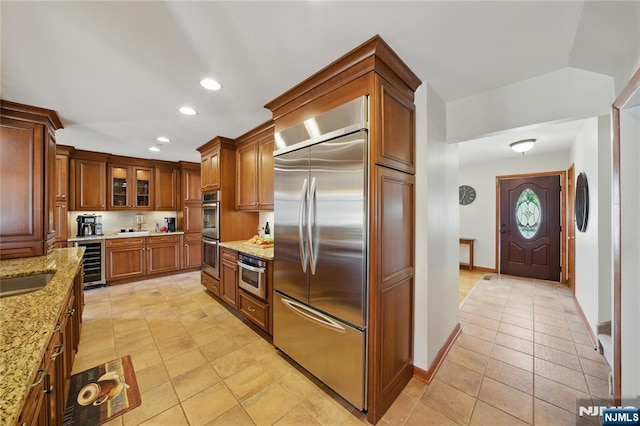 kitchen featuring light stone counters, light tile patterned flooring, beverage cooler, stainless steel appliances, and brown cabinetry