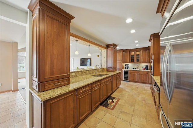 kitchen with wine cooler, appliances with stainless steel finishes, brown cabinetry, a sink, and light stone countertops