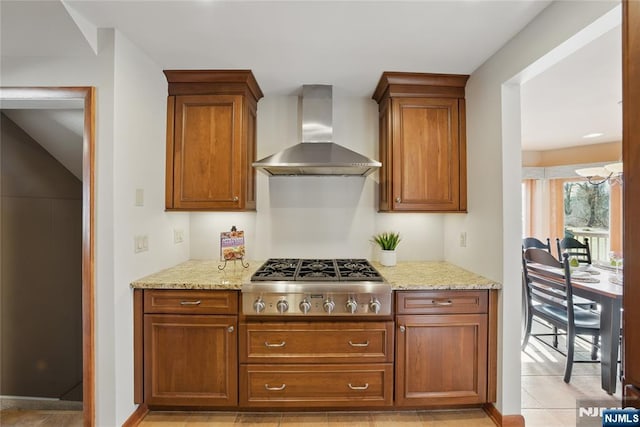 kitchen featuring light stone countertops, wall chimney range hood, stainless steel gas stovetop, and brown cabinets