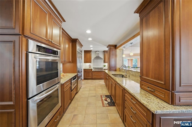 kitchen featuring light stone countertops, stainless steel appliances, wall chimney range hood, a sink, and recessed lighting