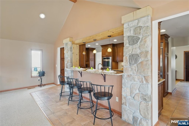 kitchen with light stone counters, pendant lighting, brown cabinets, a breakfast bar area, and high vaulted ceiling