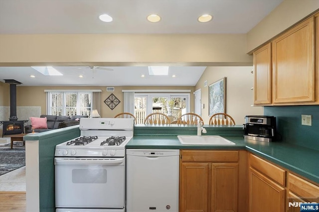 kitchen featuring white appliances, a skylight, a peninsula, a wood stove, and a sink