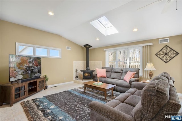 living room with a wood stove, lofted ceiling with skylight, visible vents, and baseboards