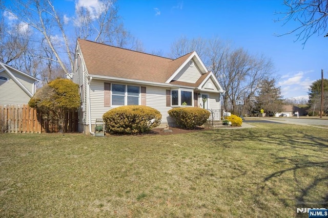 view of front facade with roof with shingles, fence, and a front lawn